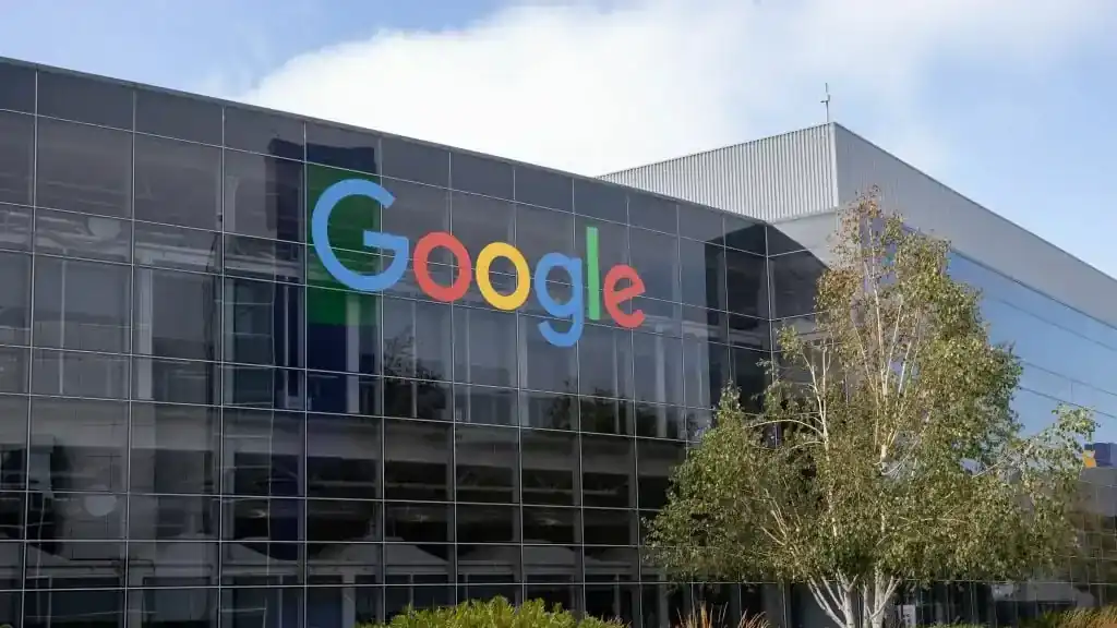 Exterior view of the Google offices in Sydney, featuring a modern glass building with the colorful Google logo prominently displayed on the facade, surrounded by greenery and a clear sky.